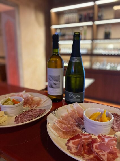 A table with plates of cured meats, a bottle of wine, and a bowl of fruit. 2