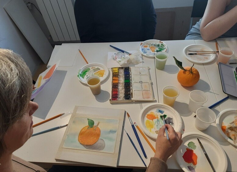 A painting activity with a watercolor palette, brushes, and a painting of an orange. 2