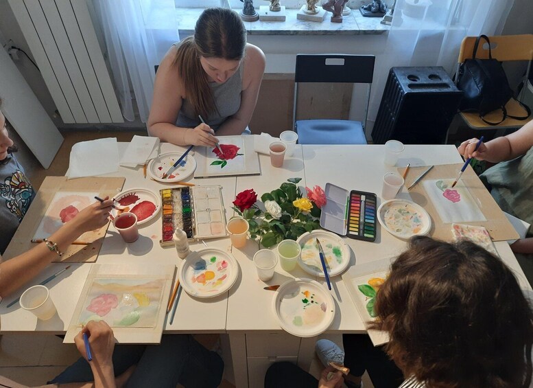 A group of people painting at a table with various art supplies. 4