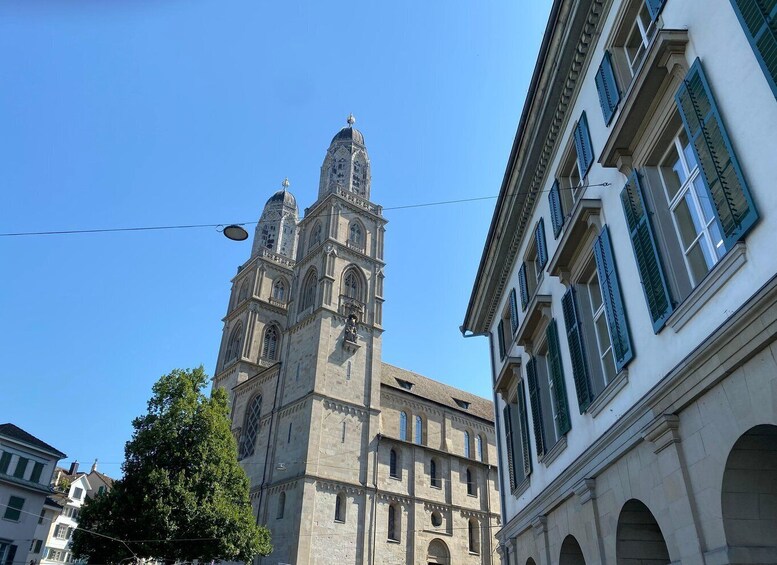 A historic church with two towers and a large central dome, surrounded by modern buildings with green shutters. 1