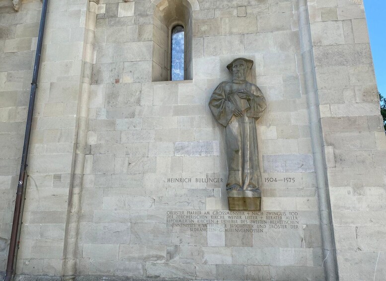 A stone statue of a man with a cross, inscribed with 'Heinrich Bullinger 1504-1575' and a German inscription below. 5