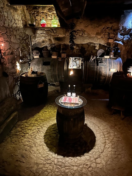 A cellar with stone walls, wooden barrels, and a table with bottles and glasses. 1