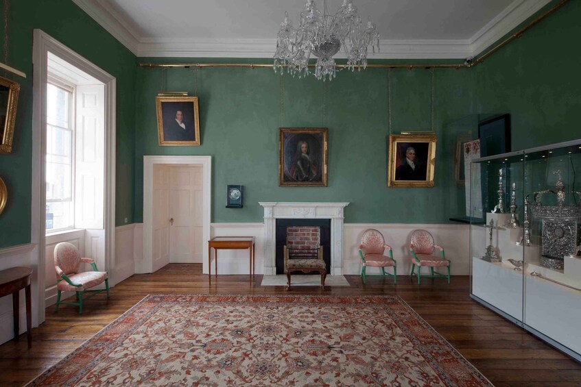 A room with green walls, a chandelier, a fireplace, and a large rug. 3