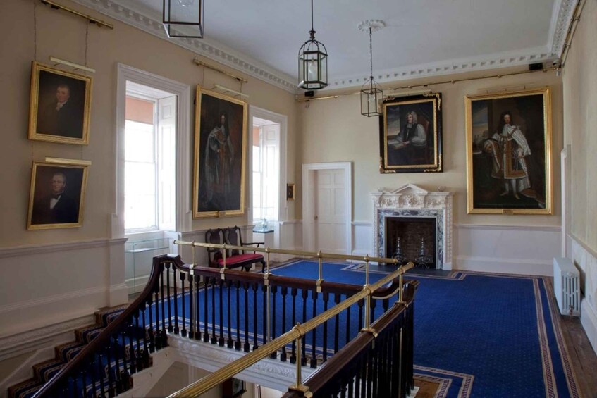 A grand room with classical architecture, featuring a blue carpet, a fireplace, and several portraits on the walls. 4