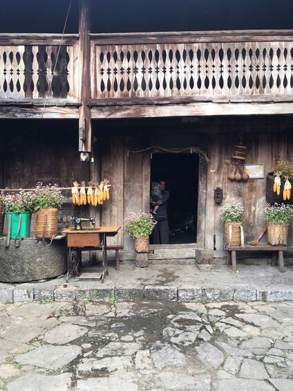 A rustic wooden building with a balcony, a sewing machine, and various potted plants. 3