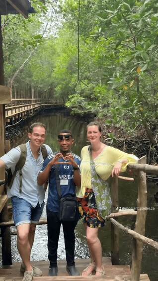 Three people on a wooden bridge over water, surrounded by dense greenery. 3