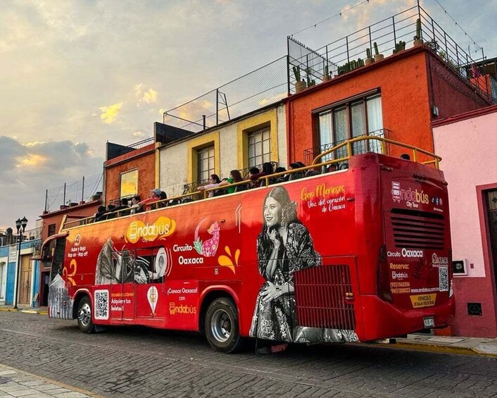 A red double-decker bus with advertisements and a QR code, parked on a street with buildings in the background. 1