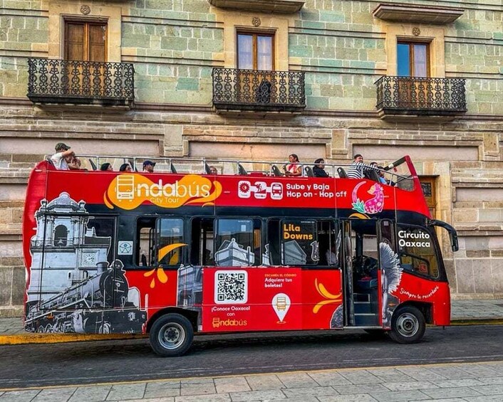 A red and black bus with advertisements and QR codes, parked on a street with buildings in the background. 4