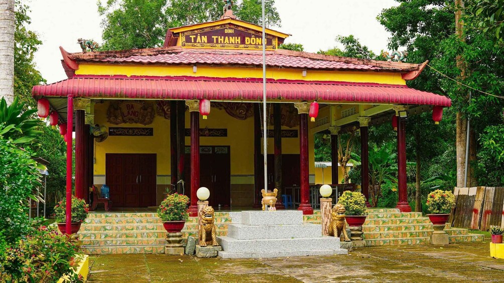 A traditional temple with a red roof, golden statues, and a sign reading 'TAN THANH DON'. 1