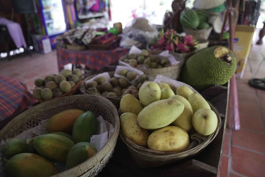 A market stall with various fruits and vegetables, including baskets of green and yellow fruits, possibly mangoes and papayas, and a large green fruit that could be a jackfruit. 5