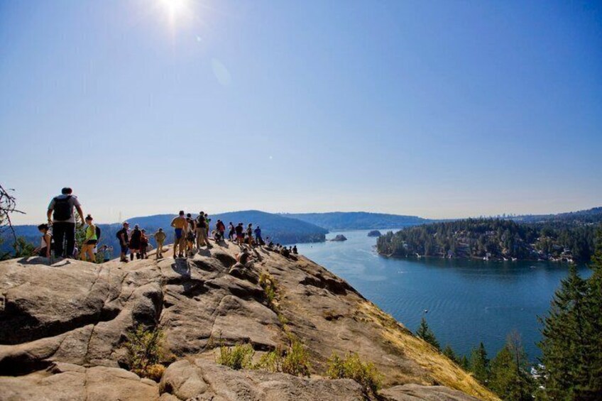 A rocky overlook with people hiking, a lake, and distant mountains. 2