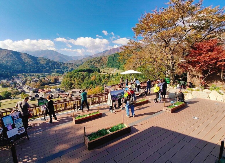 A scenic overlook with people enjoying the view, wooden deck, and autumn foliage. 3