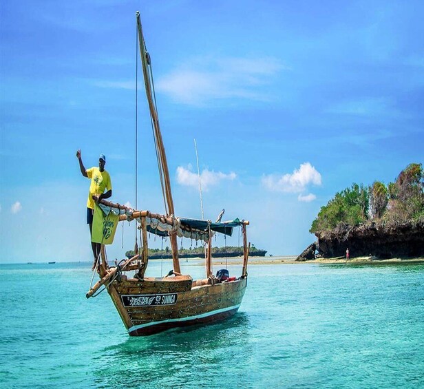 A traditional wooden boat with a person standing on the bow, a clear blue sky, and calm turquoise waters. 5