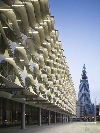 A modern architectural structure with a unique wave-like facade and a prominent skyscraper in the background. 2