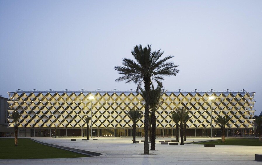 A modern building with a geometric facade, palm trees, and a well-lit plaza. 3
