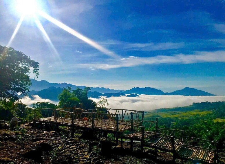 A wooden viewing platform overlooking a mountainous landscape with a view of a distant mountain and clouds below. 1