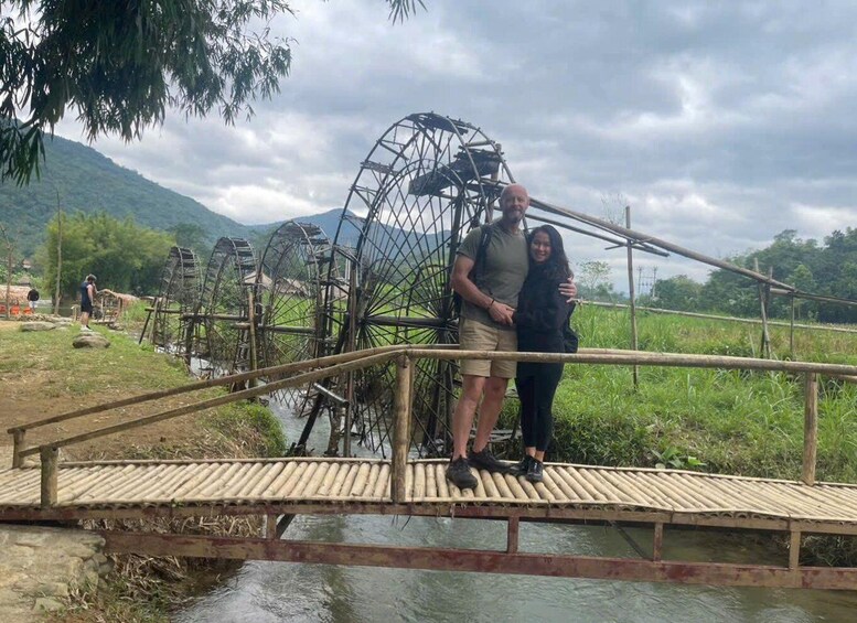 A bamboo bridge over a water body with a large water wheel structure in the background. 3