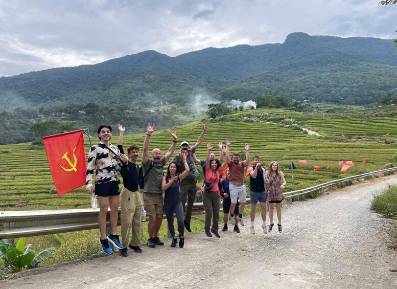 A group of people standing on a road with a red flag, surrounded by terraced fields and mountains in the background. 4