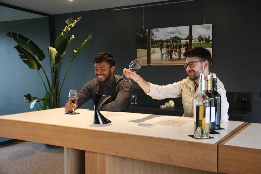 Two people toasting with wine glasses at a bar with a large plant and a framed picture on the wall. 5