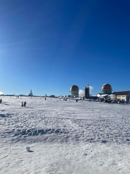 A snowy landscape with two domed structures, a statue, and a few people walking. 2