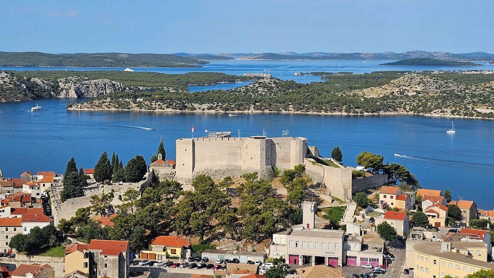 A coastal town with a prominent castle, clear blue waters, and a hilly landscape in the background. 5