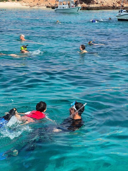 People swimming in a clear blue sea with boats in the background. 2