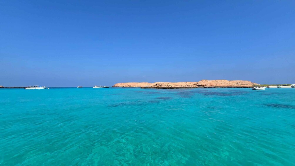 A clear turquoise sea, boats, and a rocky coastline. 5