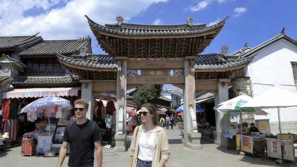 Une porte chinoise traditionnelle, ornée d’un décor complexe sur le toit, une rue animée bordée d’étals de marché et de piétons. 3