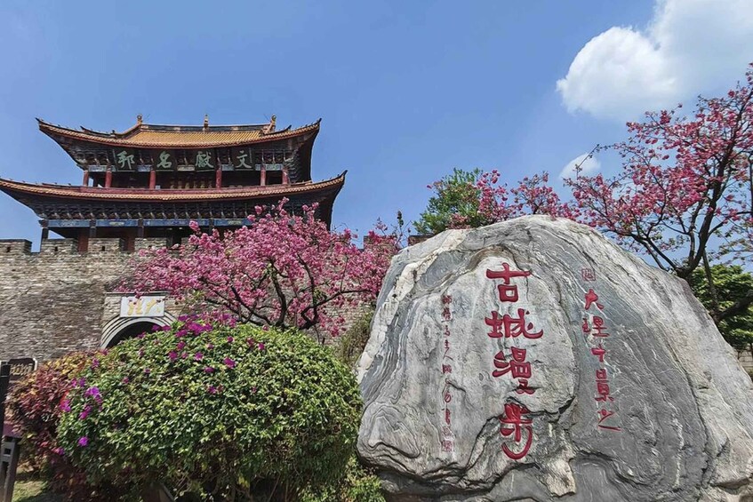 Un bâtiment traditionnel chinois doté d’un toit de style pagode, d’une grande pierre portant des inscriptions et de cerisiers en fleurs. 2