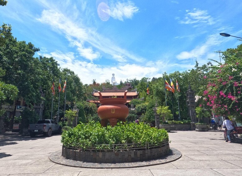 A large traditional Chinese urn in the center of a circular stone platform, surrounded by lush greenery and a clear blue sky. 2
