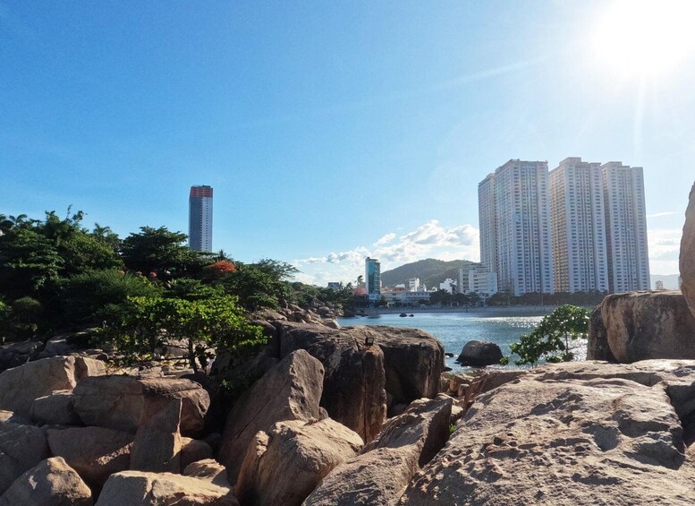 A rocky shoreline with large boulders, a clear blue sky, and high-rise buildings in the background. 5