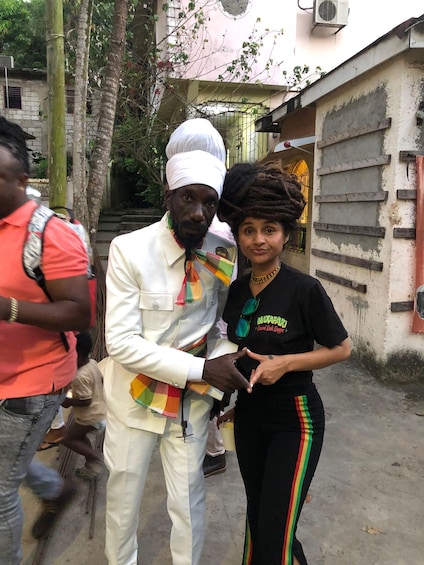 A person in a white suit with a colorful scarf, another in a black shirt with a logo, and a third in a red shirt. 2