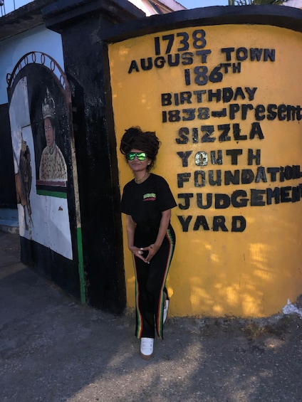 A person standing in front of a yellow wall with a mural and text. 5