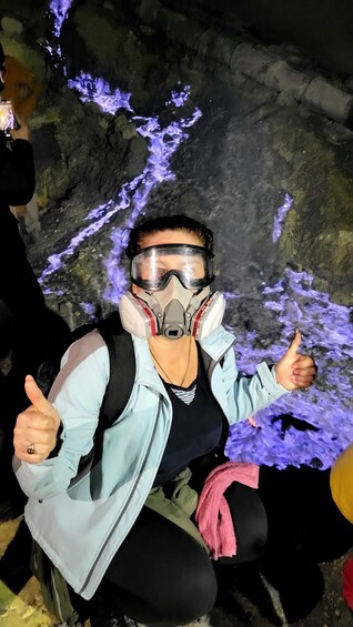 A person wearing a light blue jacket, black pants, and a face mask, giving a thumbs up. 4