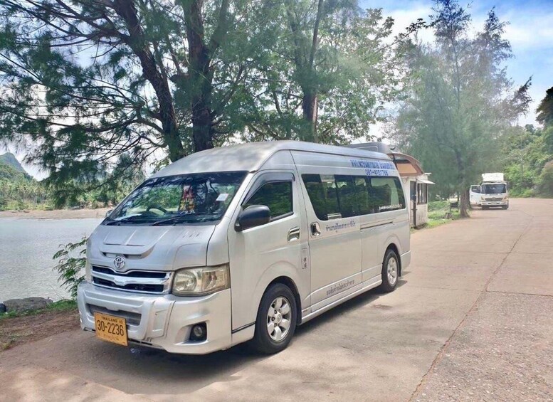 A silver van parked on a paved area with trees and a body of water in the background. 3