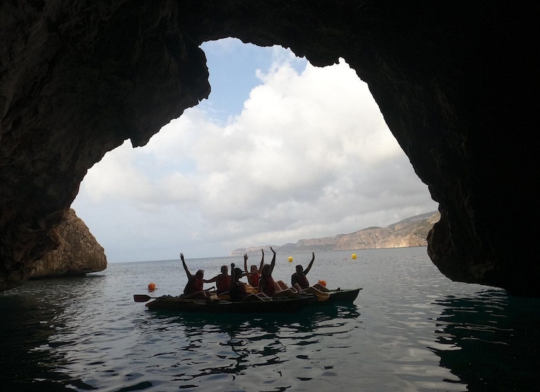 Un grupo de personas en un bote dentro de una cueva, con el mar y acantilados visibles por la entrada. 5