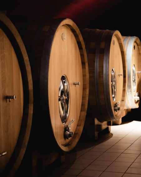Wooden wine barrels with metal fittings, arranged in a row on a tiled floor. 2