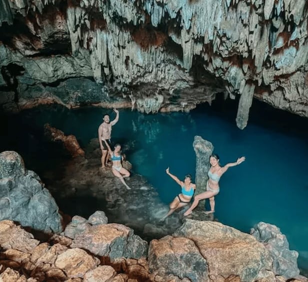 A cave with stalactites and stalagmites, a pool of water, and people jumping into the water. 5