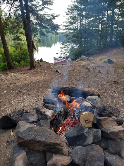 A campfire surrounded by rocks, a lake, and trees in a forest. 1