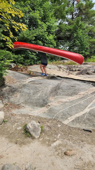 A person carrying a red canoe over rocks in a forested area. 4