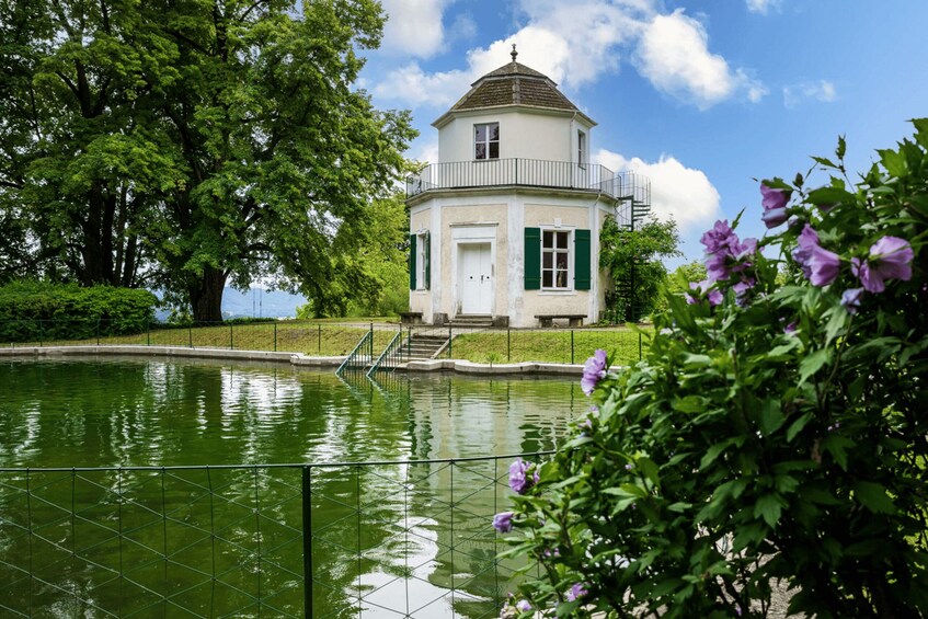 A white building with green shutters, a small staircase, and a pond in front. 3