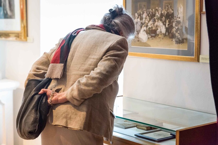 A person in a beige coat and black handbag standing in front of a glass display case with books and framed photographs. 5