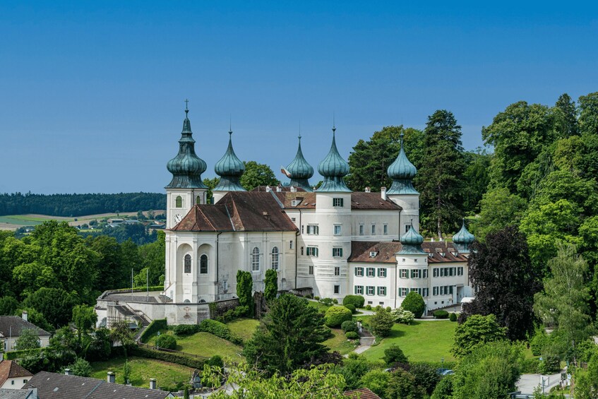 A large white building with multiple green domed towers, surrounded by lush greenery and a clear blue sky. 2