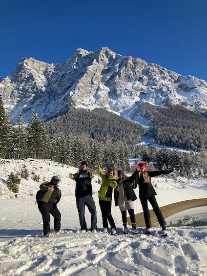 A group of people posing on a snowy mountain with a clear blue sky and snow-covered trees in the background. 2