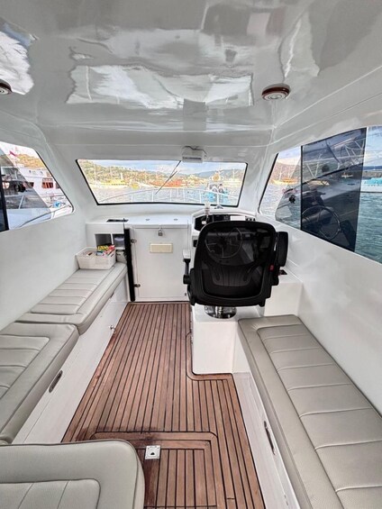 A boat's interior with a steering wheel, cushioned seating, and a view of a marina. 5