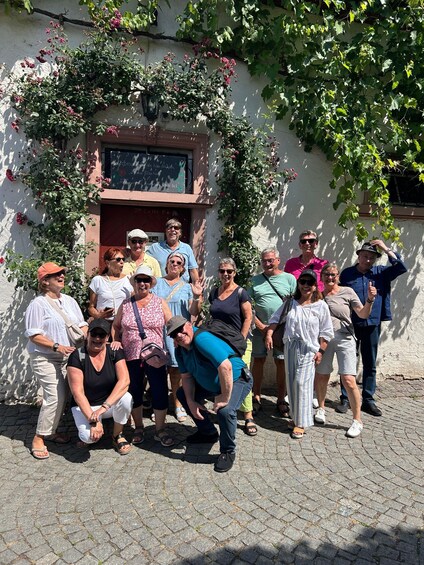 A group of people posing in front of a building with a white wall and a red door. 4
