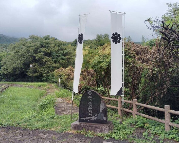 A stone monument with Chinese characters, surrounded by a wooden fence and two white banners with black floral designs. 5
