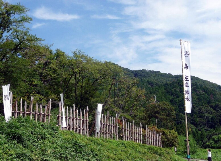 A bamboo fence with flags, a forested hill, and a clear sky. 4