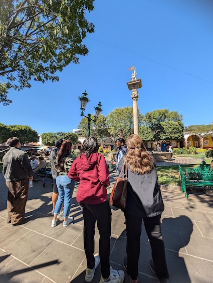 A public square with people walking, a statue, and a fountain. 2