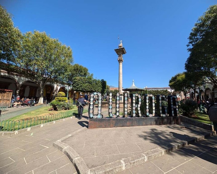 A square with a central monument, surrounded by trees and a fountain. 4